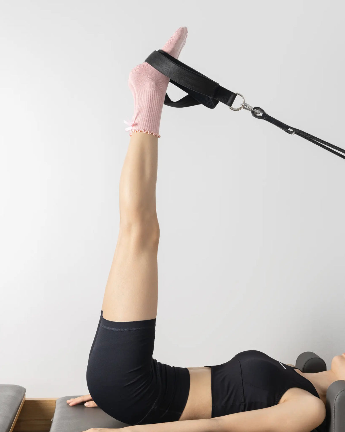 Legs extended on a reformer footbar wearing pink Tenduu Active grip socks