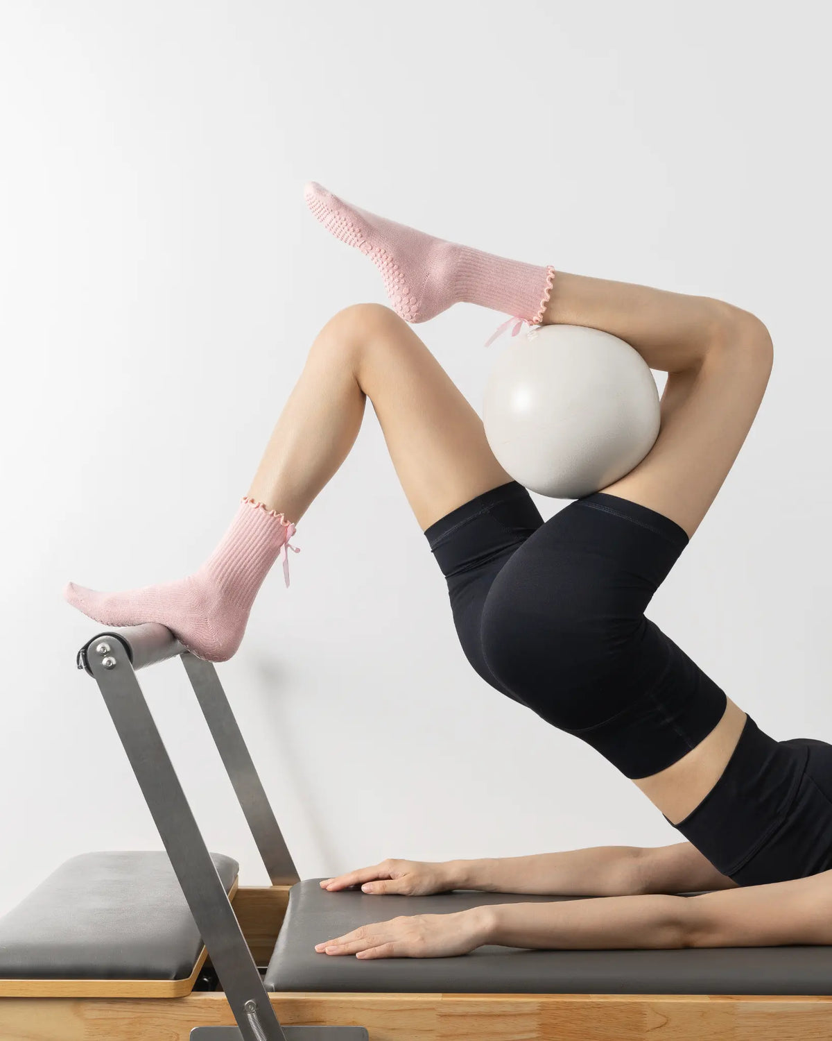 Pulling on a pink ruffled-cuff Tenduu Active grip sock before a Pilates class